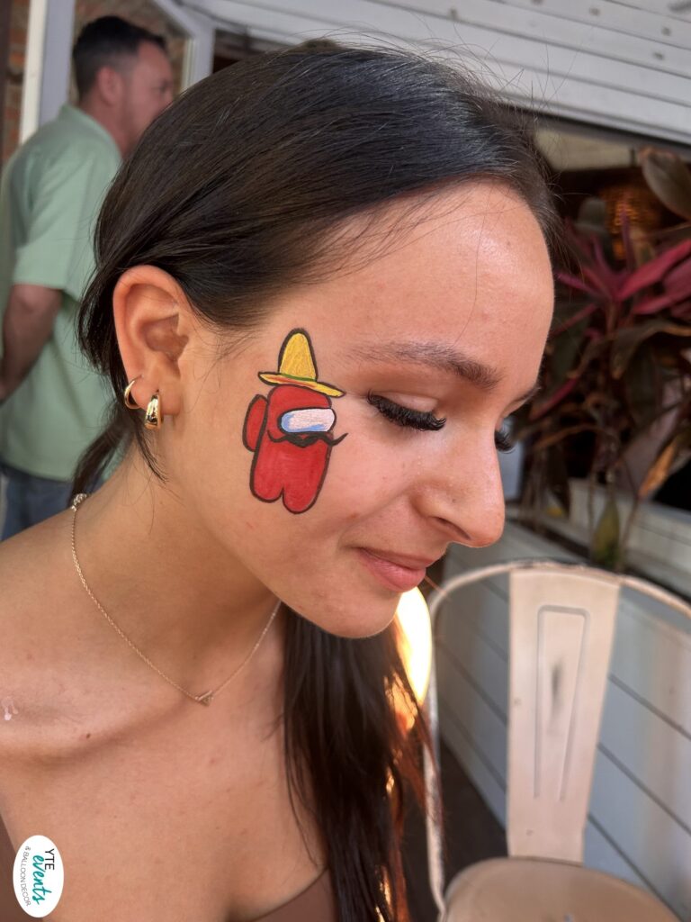 Close-up of a young woman with red Among Us character face painting wearing a yellow hat