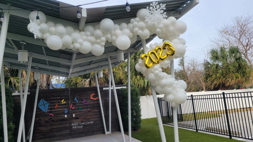 White balloons hang from the supports of an outdoor structure to form an decorative balloon arch