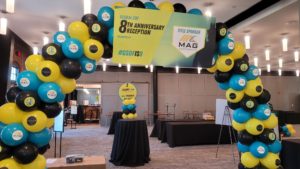 black blue and yellow balloon arch with an 8th anniversary banner, tables with black tableclothes in the background