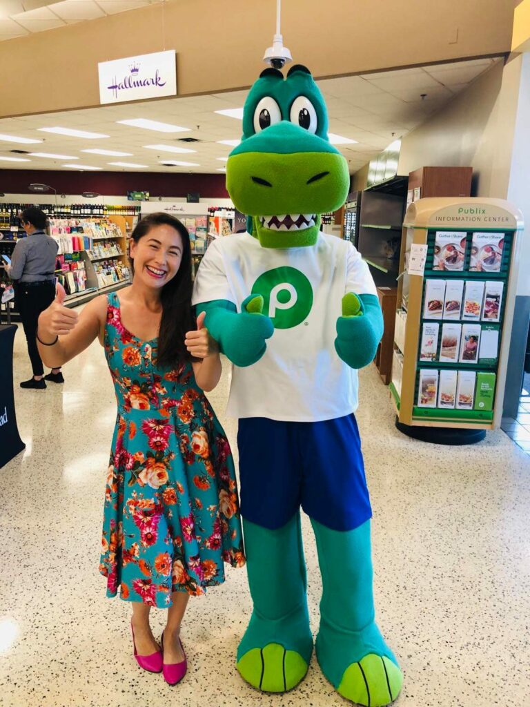 woman in green dress with alligator mascot at publix brand store promo event
