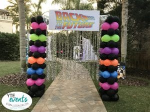 Back to the future themed entrance with silver tassels and neon columns of balloons