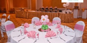 Balloon centerpiece of a pink and white flower with a green stem in a banquet hall .