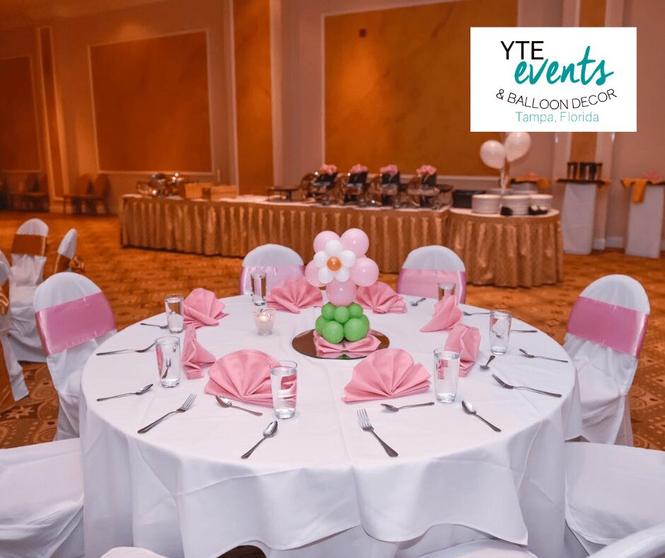Balloon centerpiece of a pink and white flower with a green stem in a banquet hall .