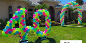 Balloon decor including a pair of balloon sculptures in the shape of the number forty and a balloon arch all made from green blue pink and yellow balloons.