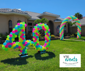 Balloon decor including a pair of balloon sculptures in the shape of the number forty and a balloon arch, all made from green, blue, pink, and yellow balloons.