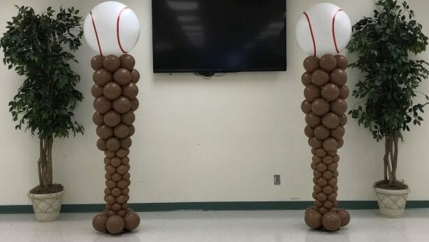 Baseball themed stage decor with column sculptures shaped like baseball bats and baseball topper
