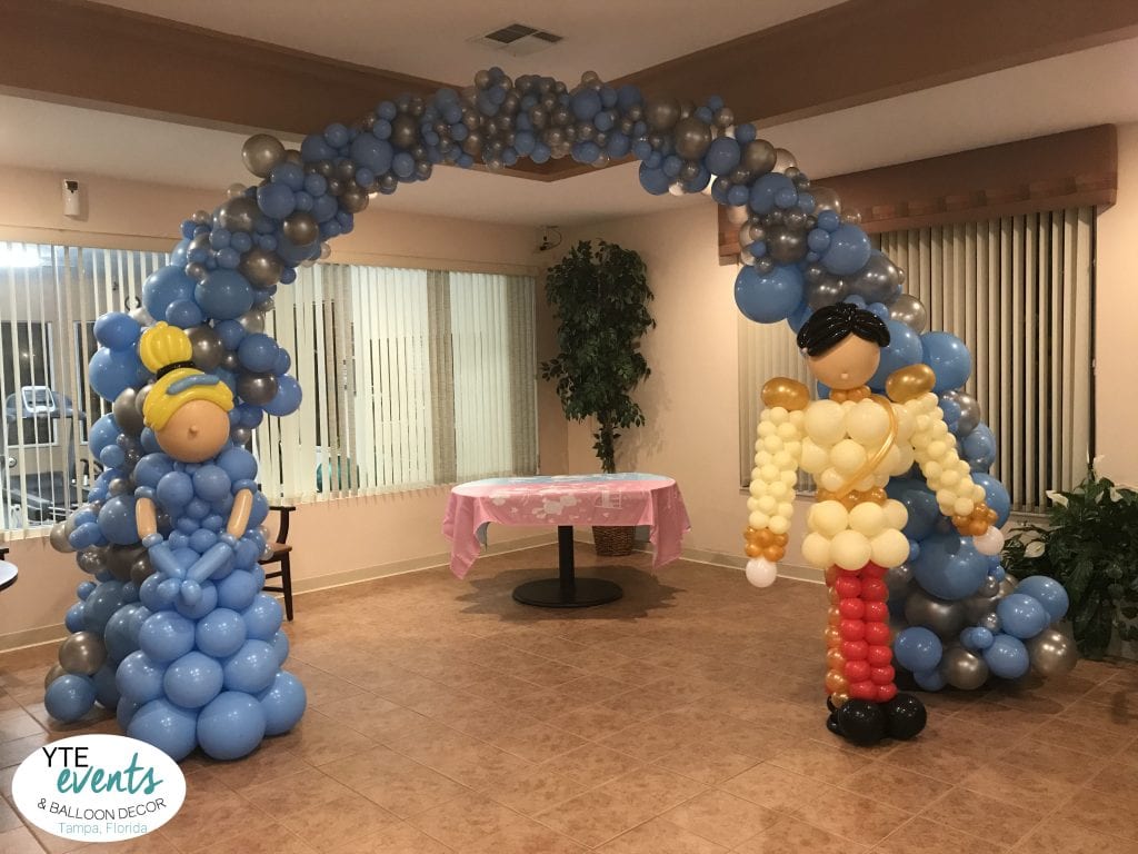 Cinderella sculpture and prince charming sculpture for baby shower in front of arch organic tapered decorations over cake table