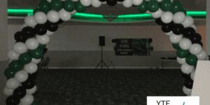 Green white and black balloon archway at the entrance to a dimly lit dance party.