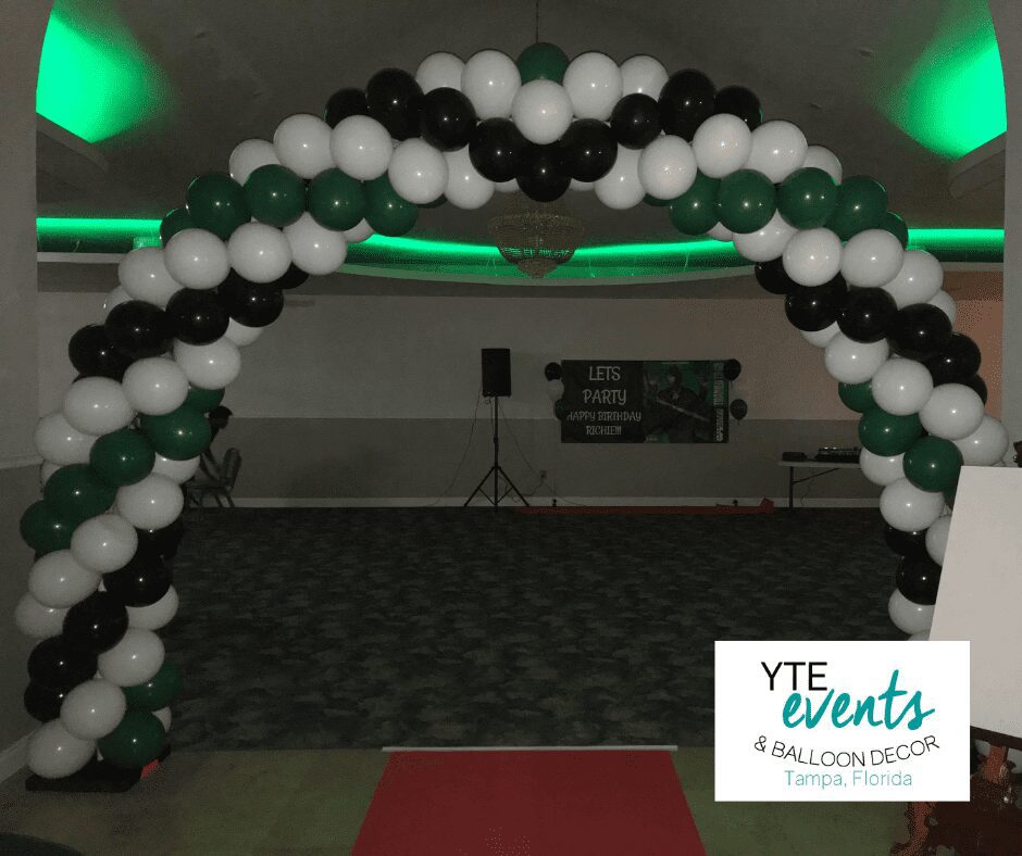 Green white and black balloon archway at the entrance to a dimly lit dance party.