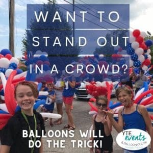 Group of people with balloon decor on their backs and heads standing out in a crowd at a parade. scaled