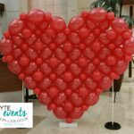 Heart shaped balloon sculpture made of red latex balloons in a building lobby.