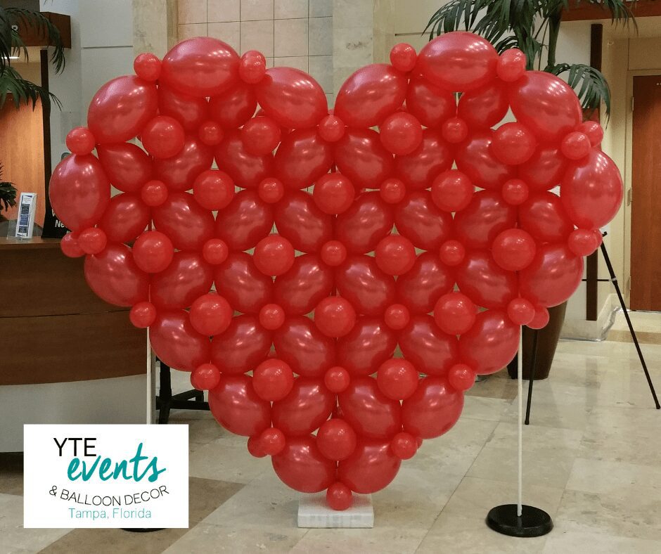 Heart shaped balloon sculpture made of red latex balloons in a building lobby.