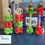 Red and green balloon columns that look like stacks of Christmas presents and topped with monkey elves made out of foil balloons.