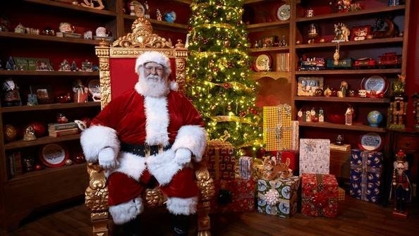 Santa in front of a christmas tree and presents