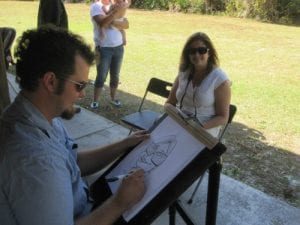 caricature artist drawing a caricature of a lady in front of him at an event outside