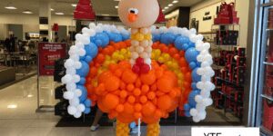 Turkey balloon sculpture made out of orange yellow blue and white balloons designed to look like a cartoon Thanksgiving turkey.