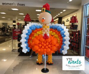 Turkey balloon sculpture made out of orange, yellow, blue and white balloons designed to look like a cartoon Thanksgiving turkey.