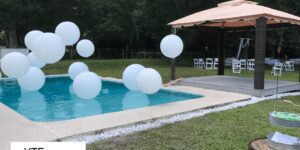White balloons strung at various heights in a pool next to a pavilion at an event.