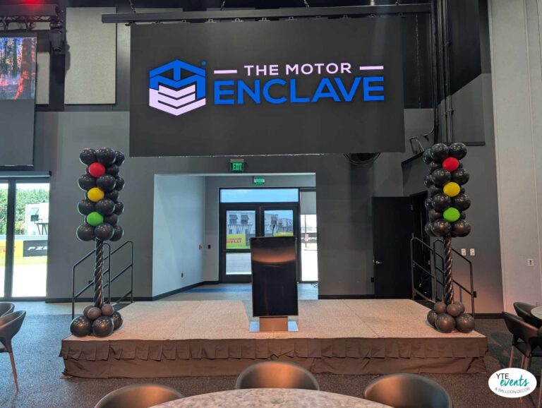 Black balloon columns with red, yellow, and green accent balloons at The Motor Enclave corporate event stage