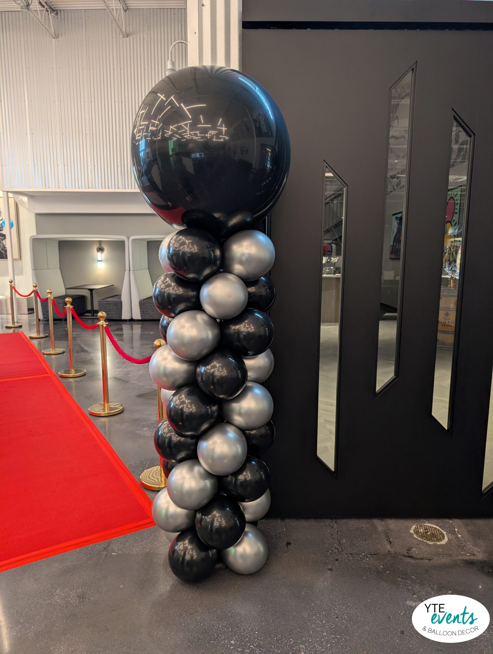 Tall black and silver balloon column with large glossy balloon on top at corporate event entrance