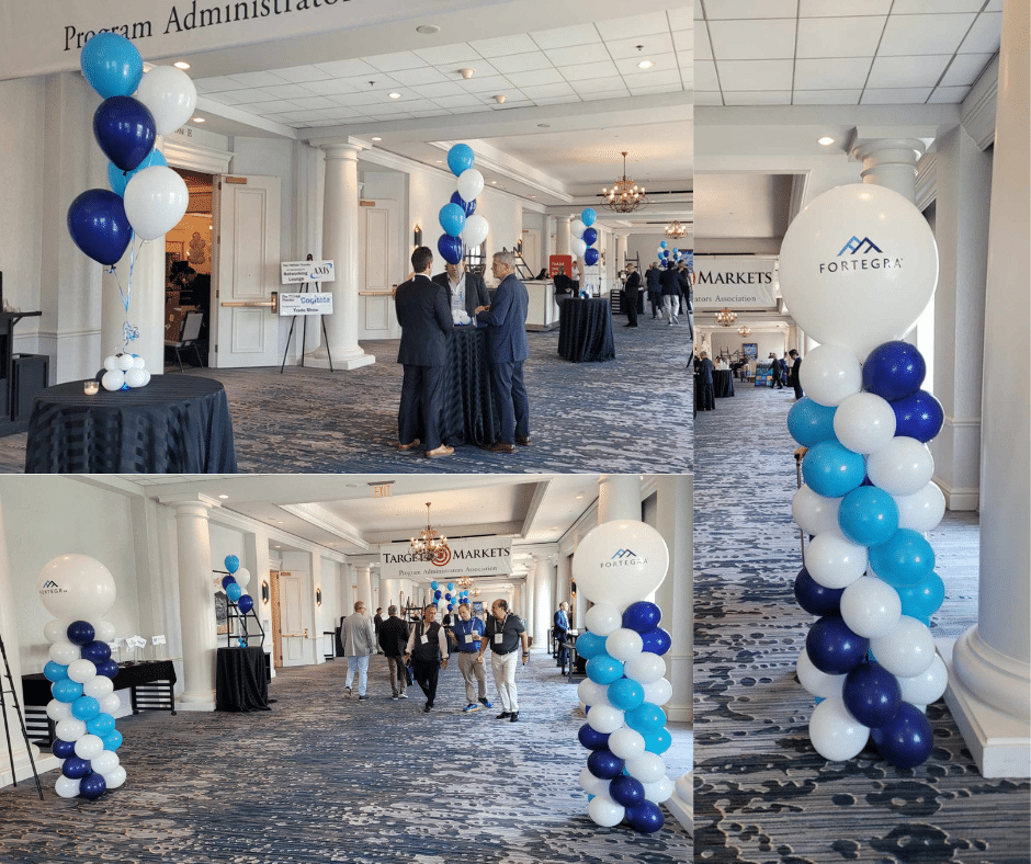 a group of people standing in a room with balloons for trade show conference highlighting balloon columns with Fortegra company name written on top of the balloon towers with towers being blue and white with bouquets of matching balloons throughout the event
