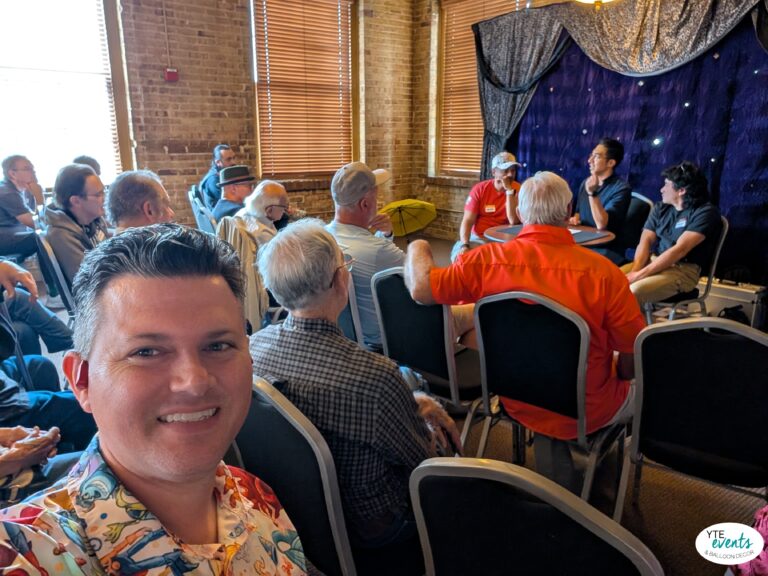Audience attentively listening to a corporate panel discussion in a brick-walled room with blinds and dark drapes