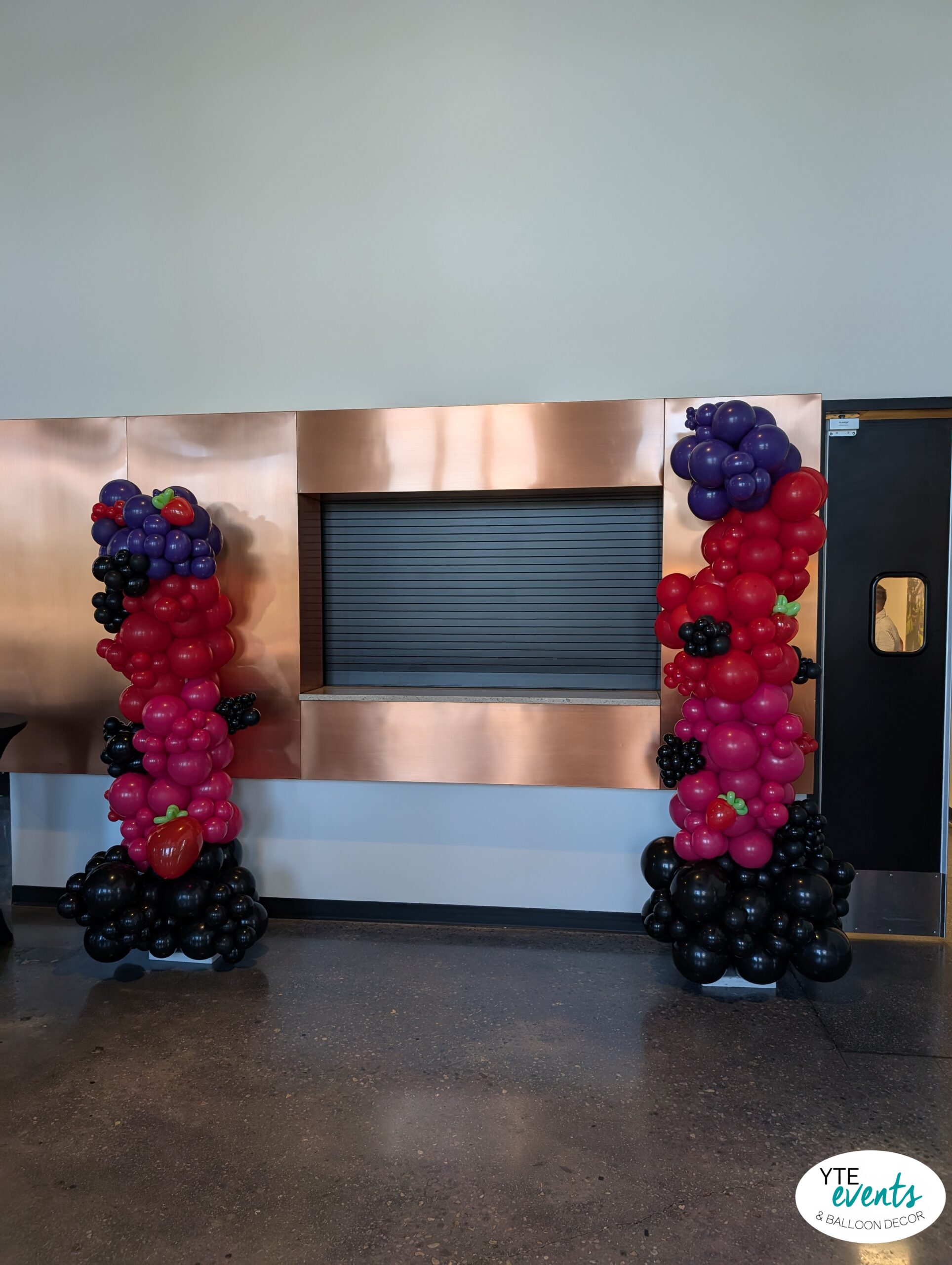 Custom balloon columns in red, black, purple with fruit-shaped balloons at corporate venue