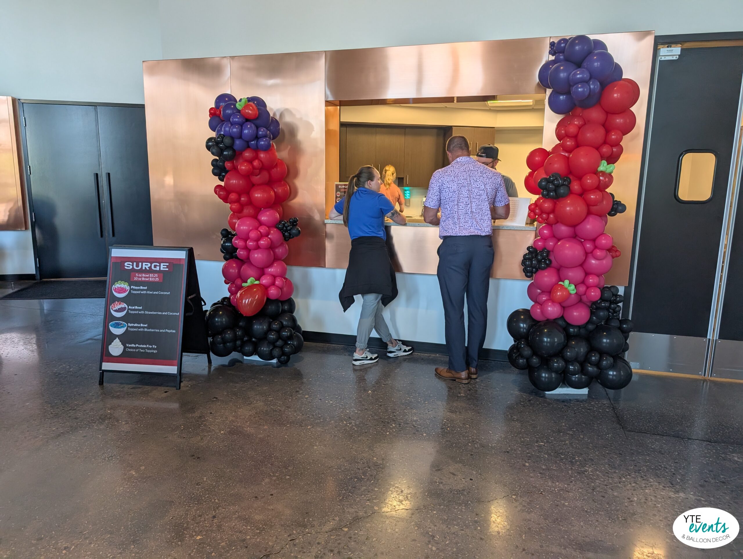 Custom fruit-themed balloon columns in red, black, purple, and pink at a corporate event serving counter