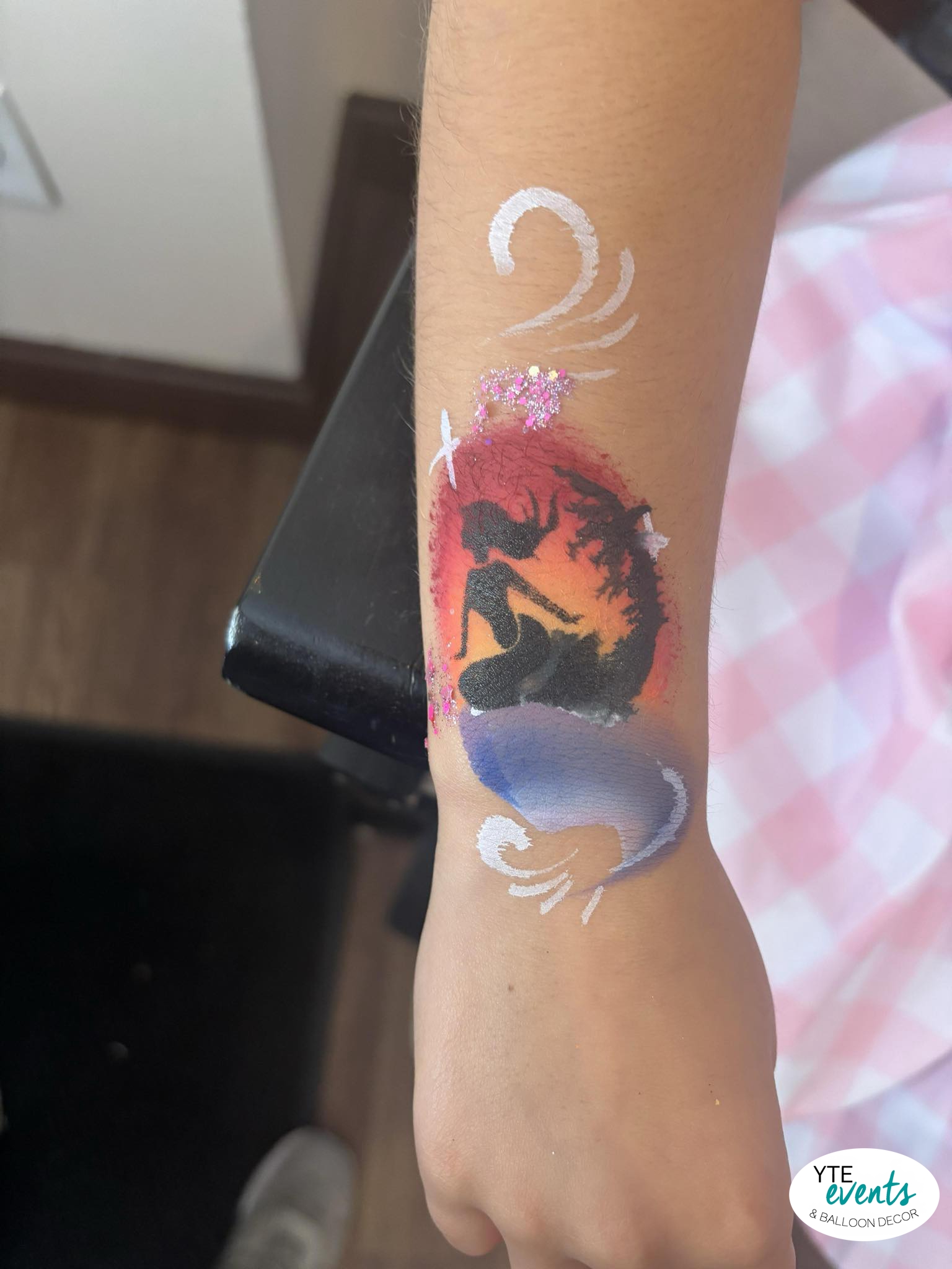 Arm with detailed mermaid silhouette body painting featuring glitter and gradient colors