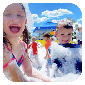 A group of joyful children immersed in a fluffy sea of foam, their faces lit up with pure delight during a professional foam party event.