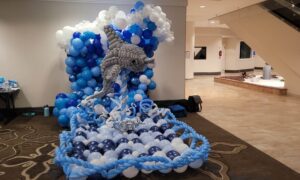 a large balloon sculpture of a dolphin and a cresting wave stands in a hallway of a convention center
