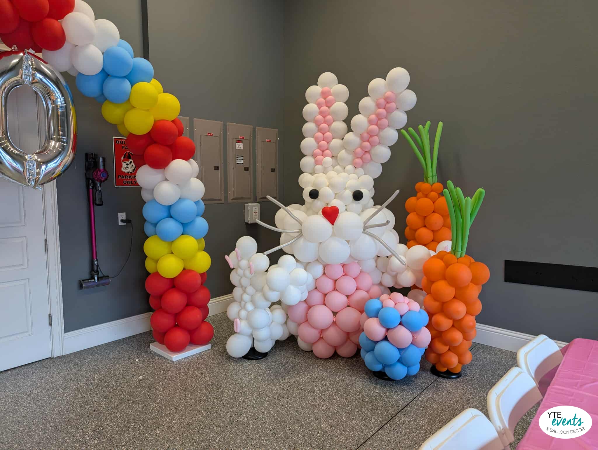 Large white and pink balloon Easter bunny with carrot balloon sculptures and rainbow balloon arch in event space