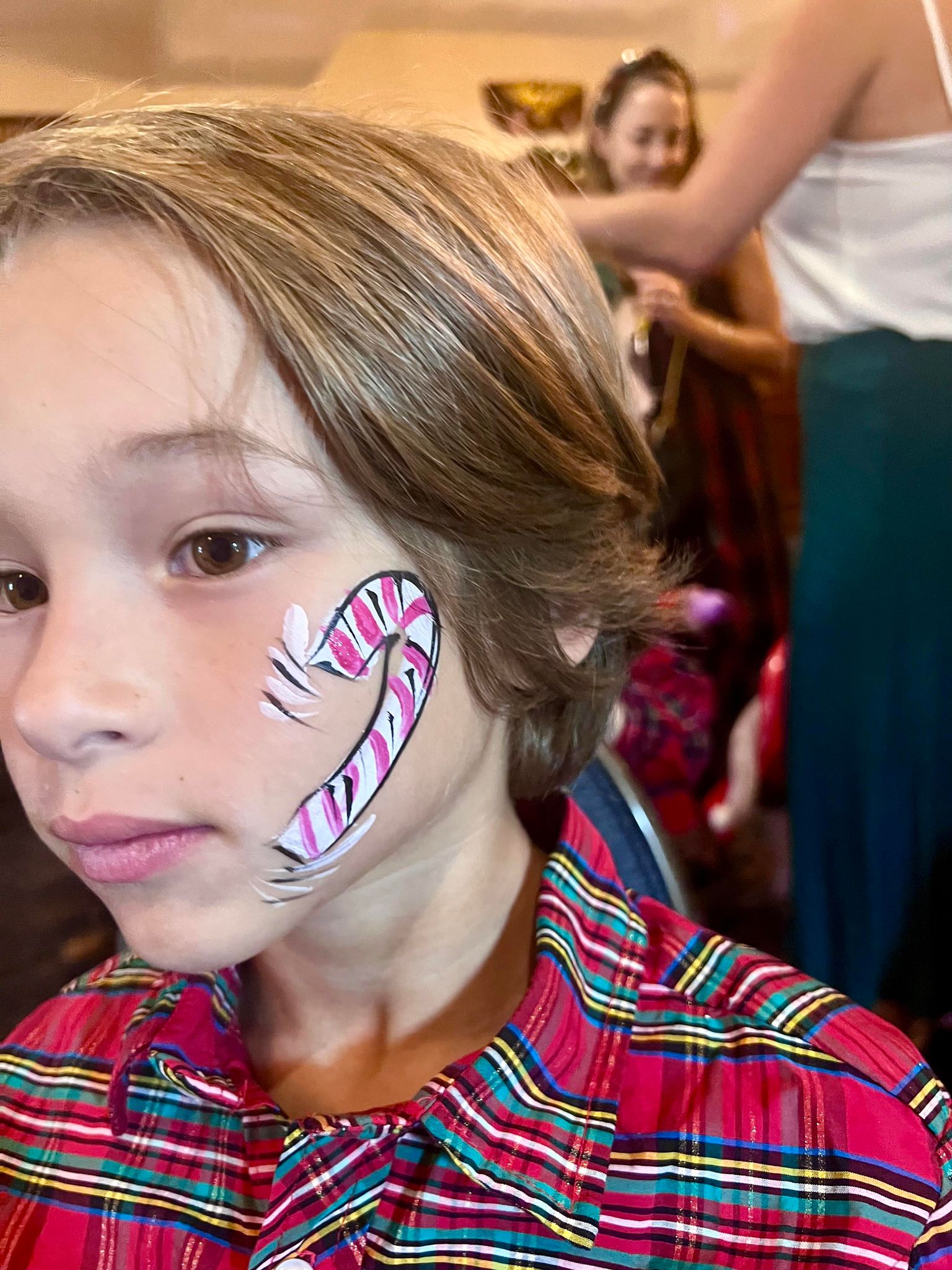 A young boy with short hair has a candy cane face painting on his cheek, displaying a festive and cheerful look.