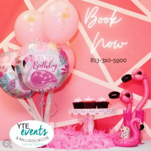 Printed flamingo balloon bundle, pink cupcakes on pedestal, twisted balloon flamingos next to feather boa, pink party setup