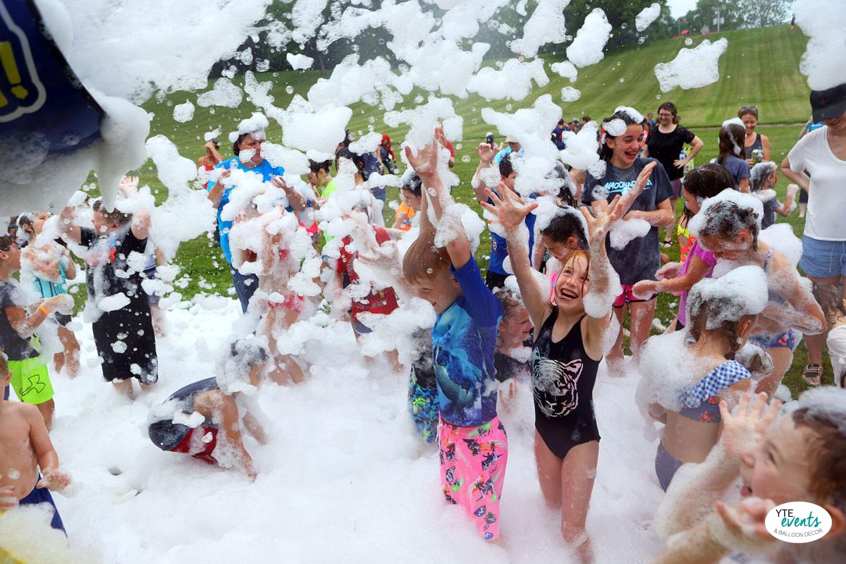 Children enjoying an outdoor foam party with lots of bubbles and foam in a grassy park