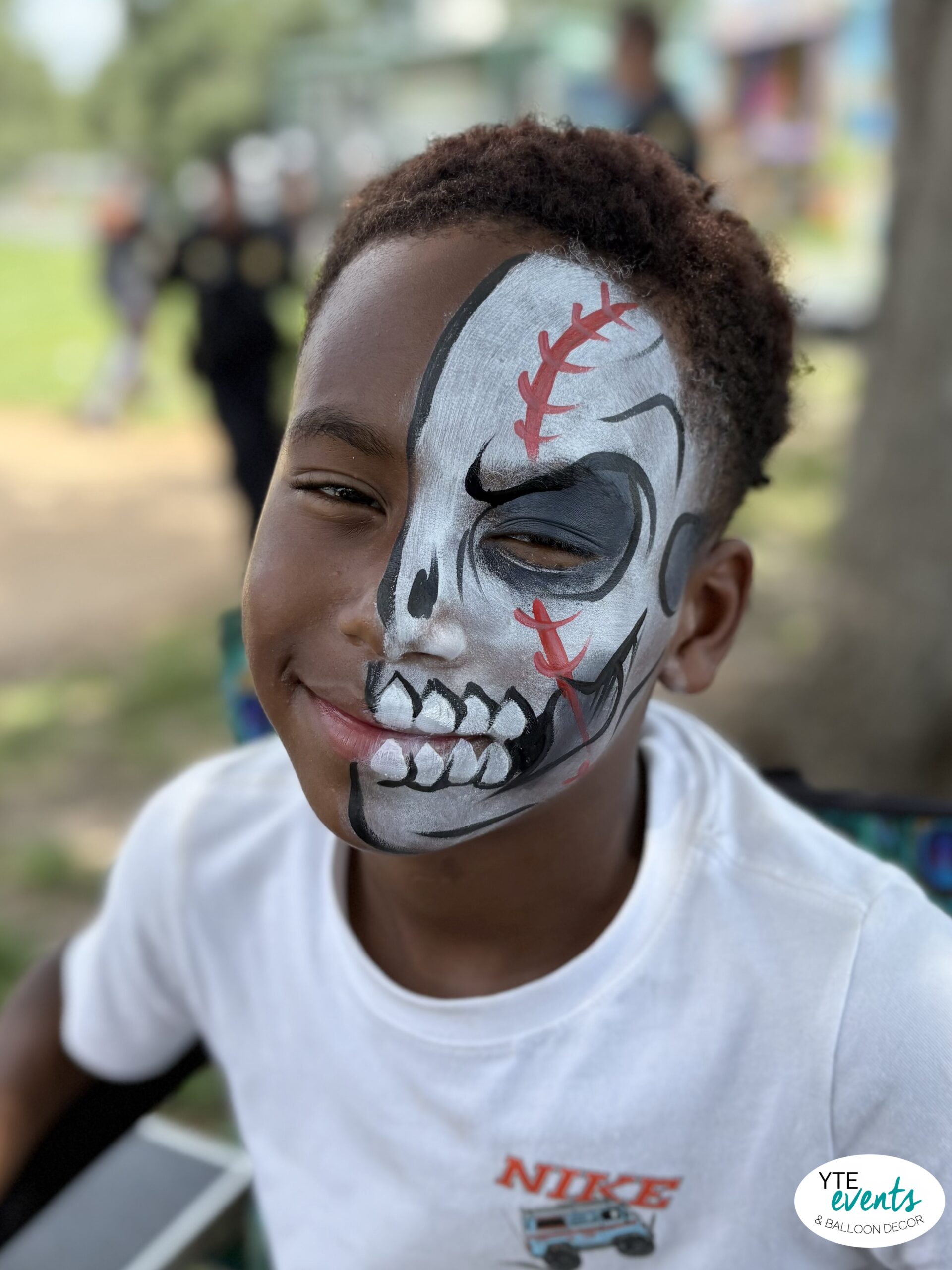 Child with half skull face painting in black, white, and red at outdoor event