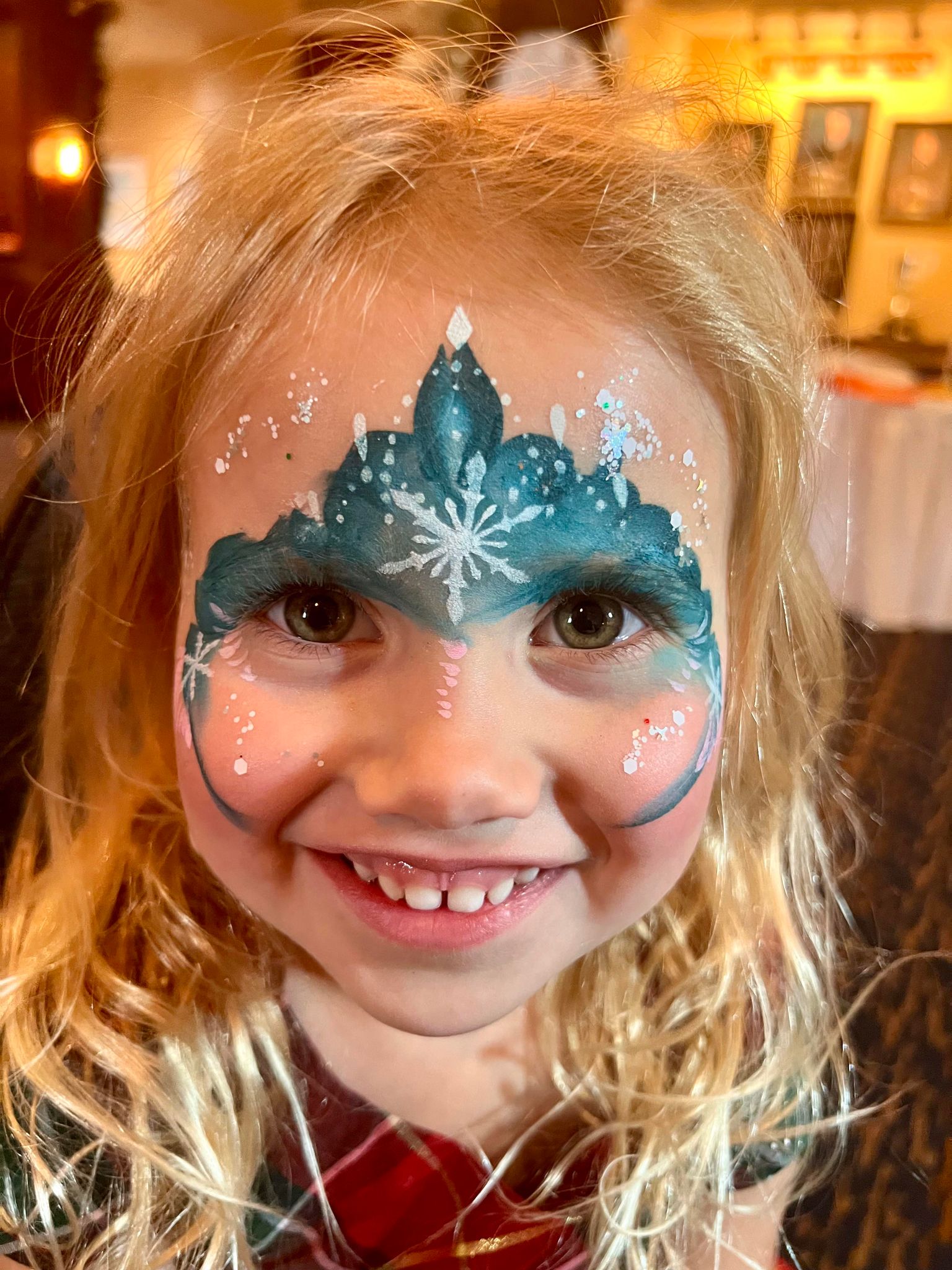 A young girl with a big smile has an intricate ice crown and snowflake face painting, adding a magical touch to her look.