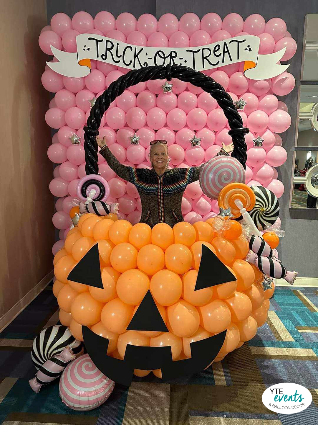 Interactive Halloween candy bucket balloon decor with orange pumpkin, black handle, and pink balloon backdrop