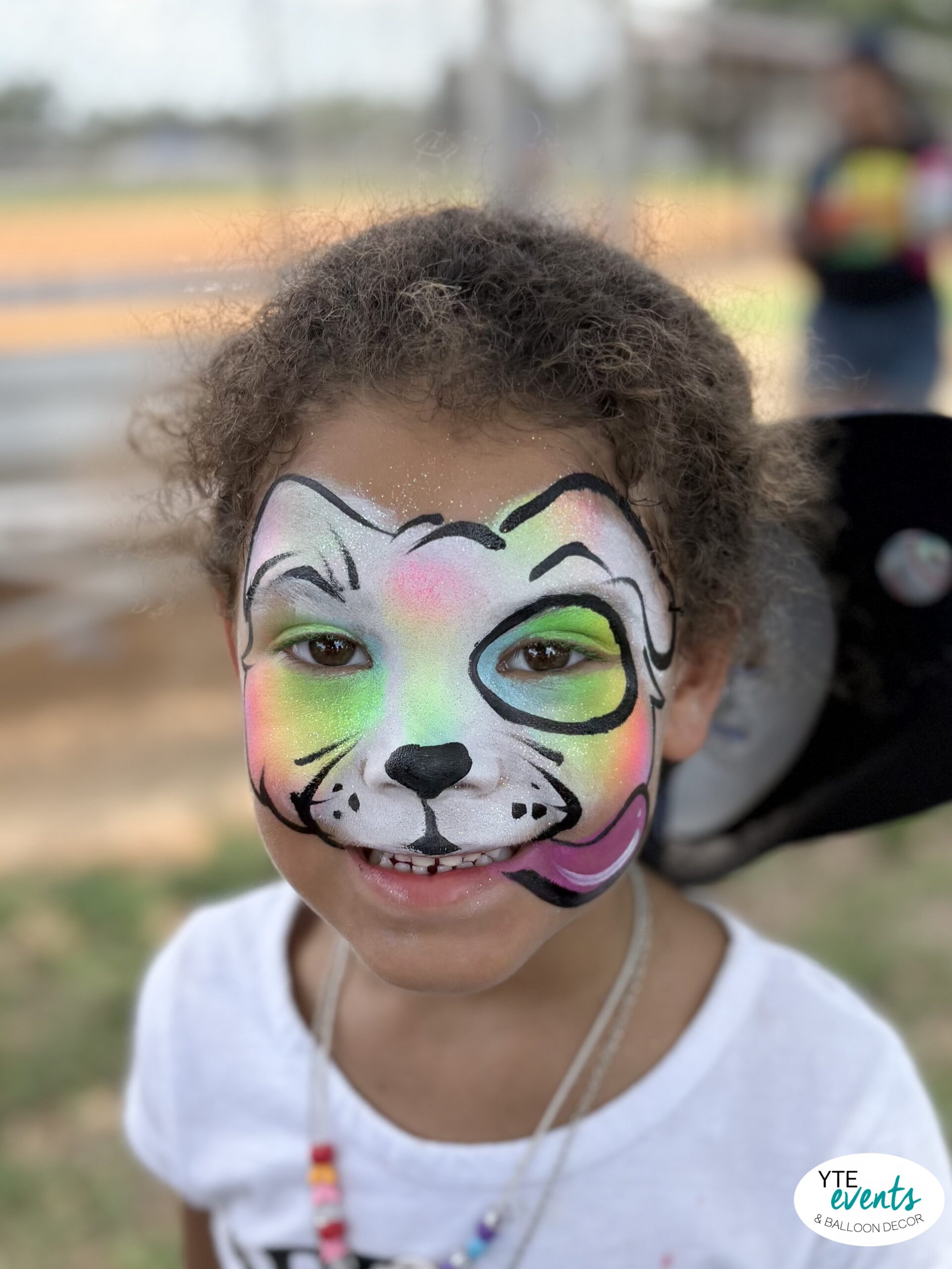 Smiling child with colorful dog face painting at outdoor event