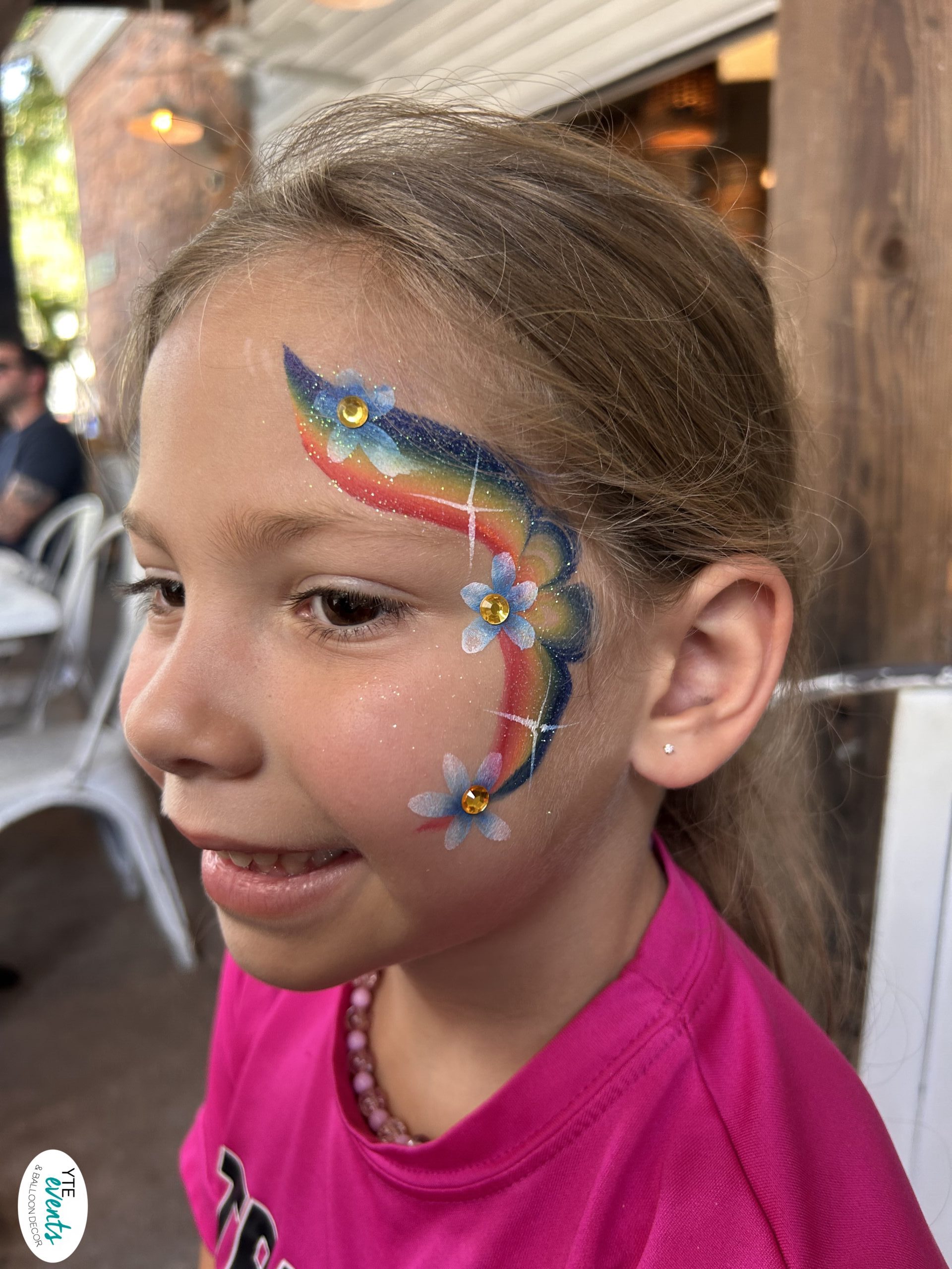 Smiling child with rainbow and flower face painting design