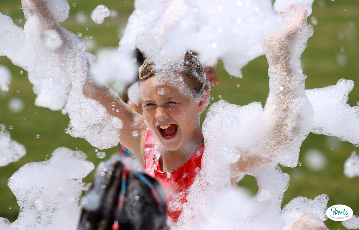 Child playing joyfully in foam bubbles at an outdoor party