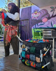 a balloon twister is creating a balloon animal while dressed as a pirate with dreadlocks and a sword.