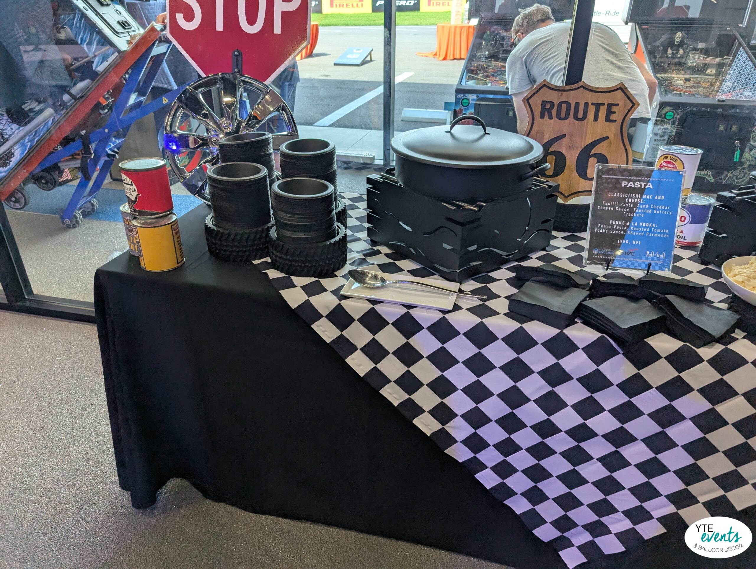 Race car themed event table with checkered flag tablecloth, tire-styled bowls, Route 66 sign, and food setup