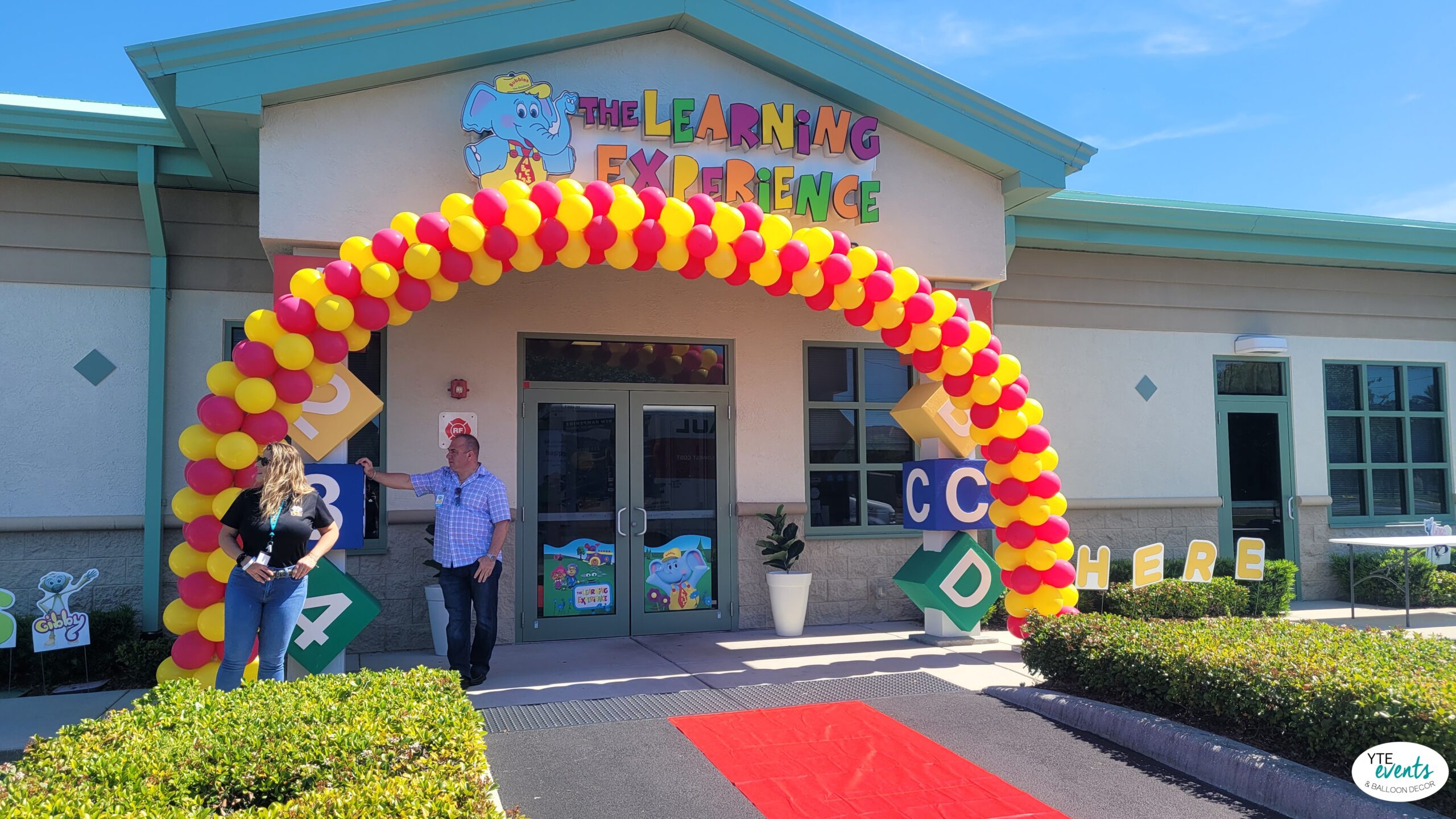 Red and yellow balloon arch decorating entrance of a kids learning center with colorful blocks and signage