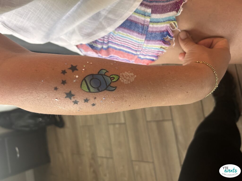 Close-up of an arm with a colorful space rocket temporary tattoo surrounded by black stars and glitter