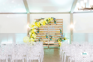 Wedding event setup with summery yellow balloon garland and pastel floral arrangements
