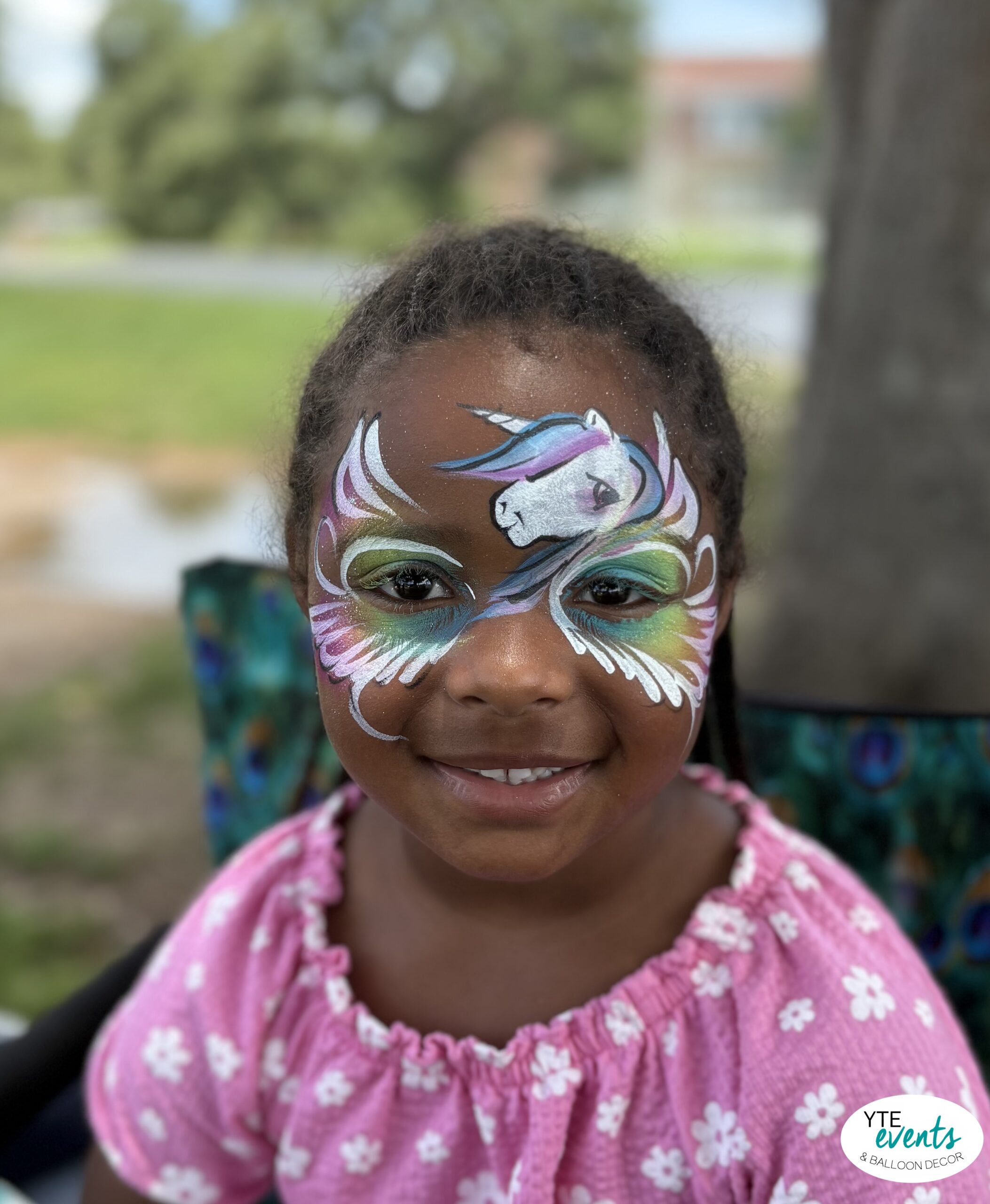 Young girl with colorful unicorn face painting at outdoor kids birthday party